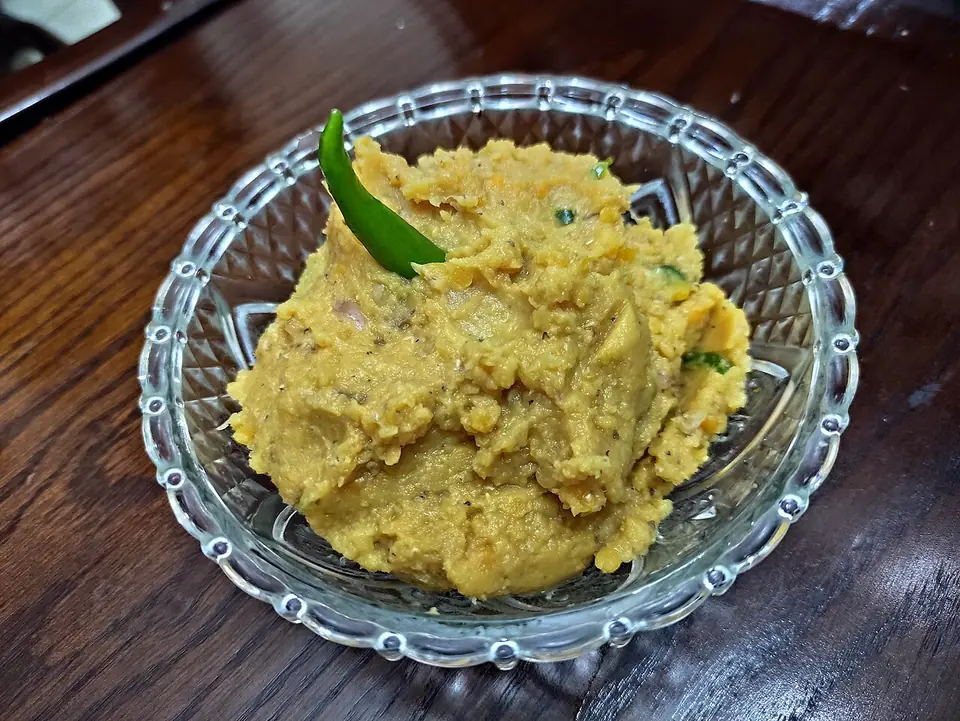 Homemade dal vorta, mashed lentils with onion and chili, in a cut-glass bowl with a green chili on top