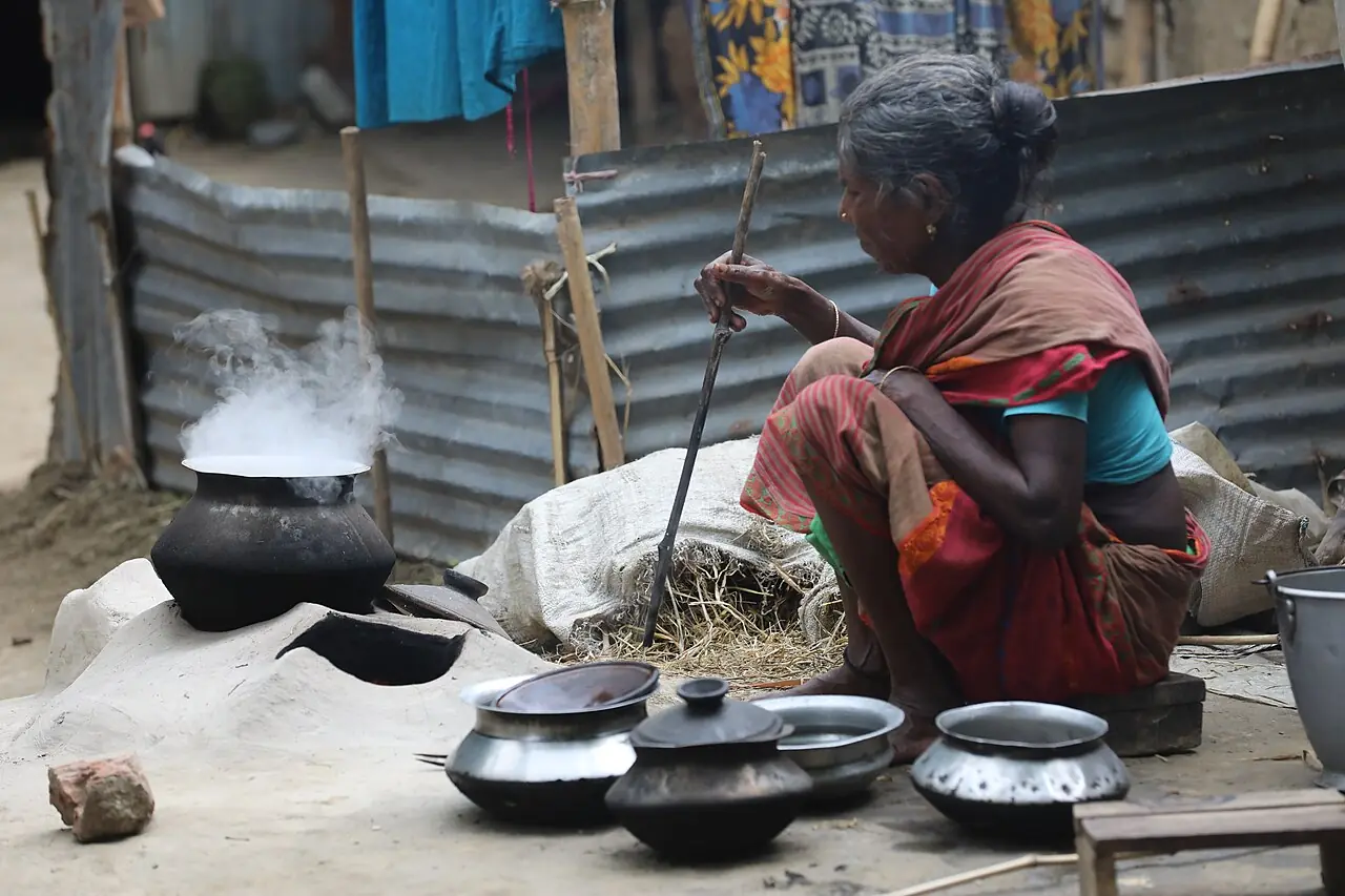 A Bangladeshi homemaker in a red sari cooking rice on a traditional clay stove